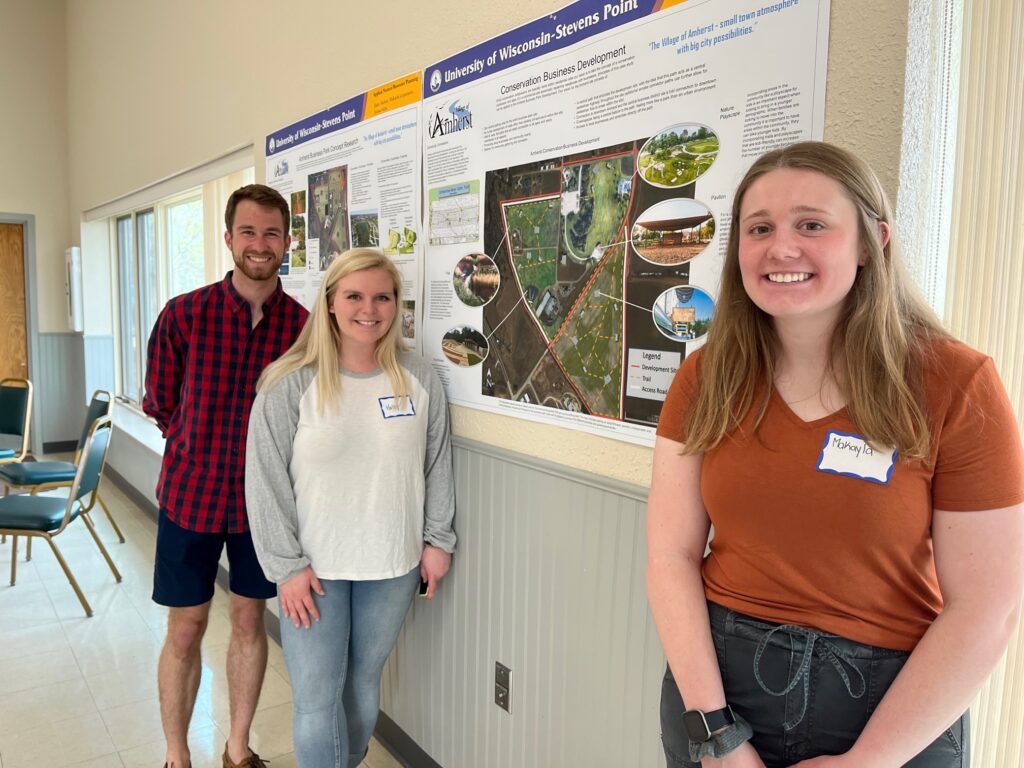 Student and community members standing next to open house poster.