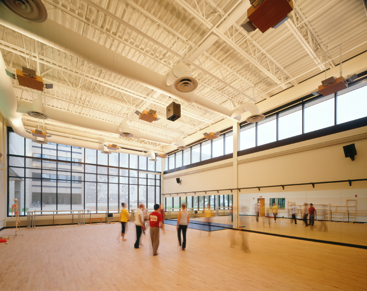 Large sunlit dance studio with four people practicing on wood floor.