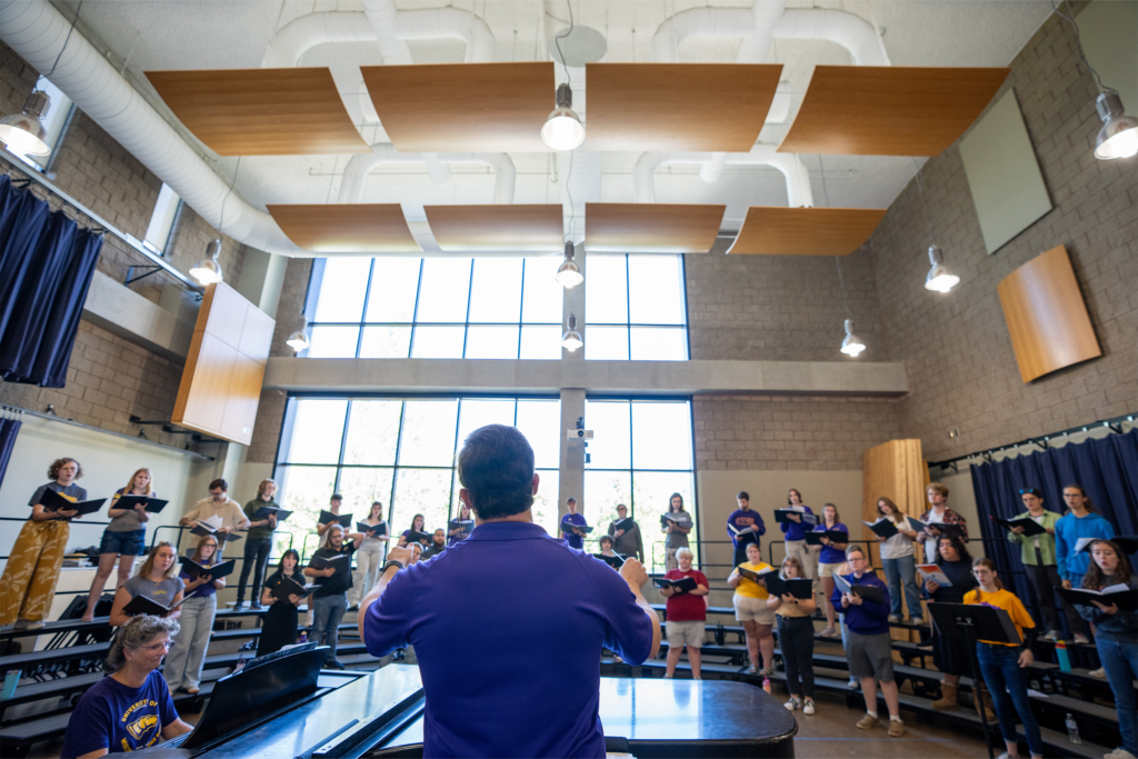 A choir rehearses indoors with singers holding sheet music together.