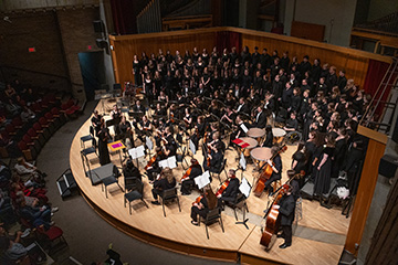 Orchestra and choir perform together on stage in concert hall.