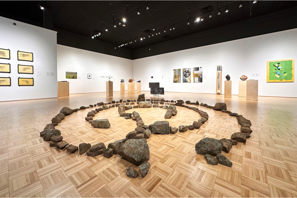 Art gallery displays stone circle installation surrounded by diverse wall artworks.