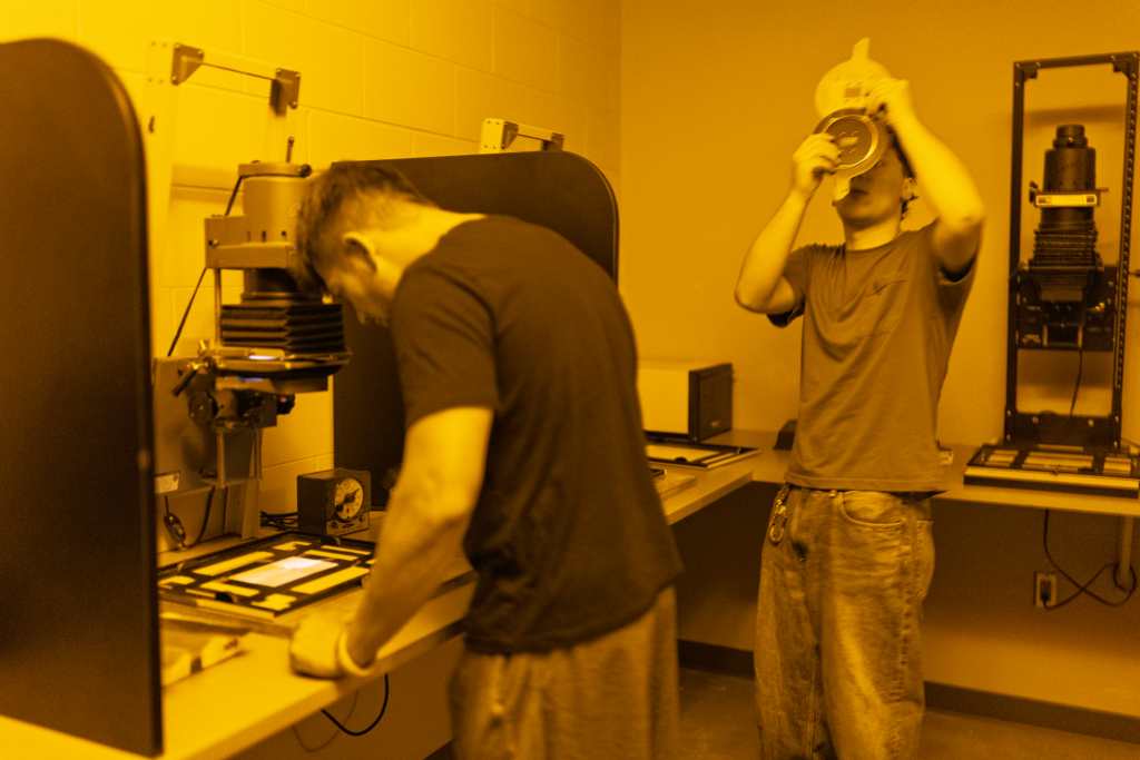 Students work in a darkroom using enlargers to process photographs.