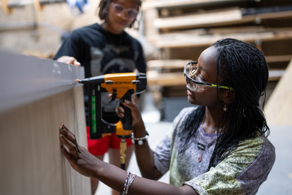 Student uses nail gun while building a wooden stage piece.