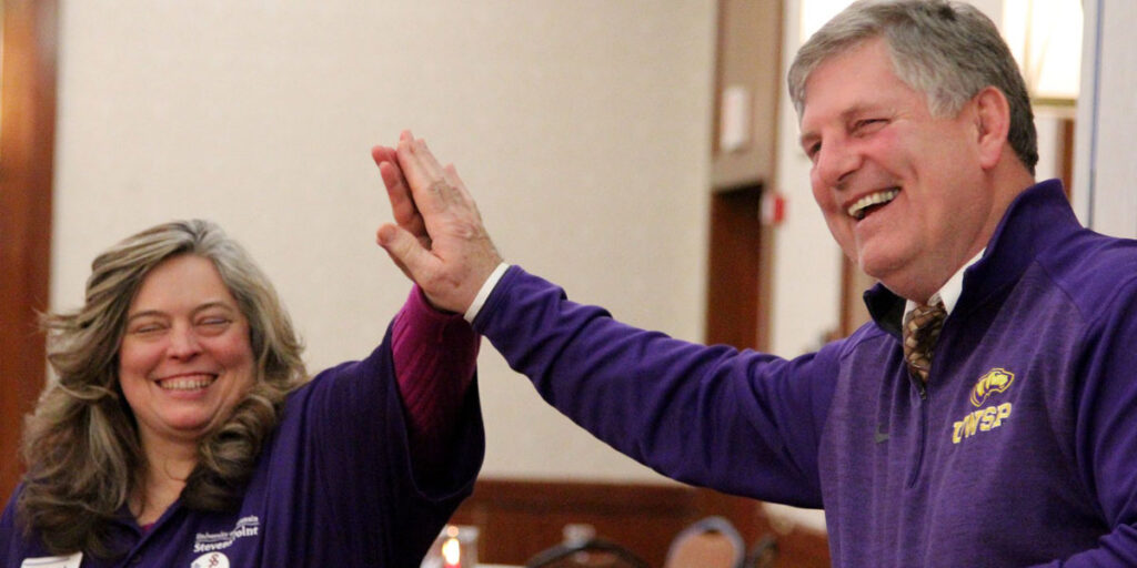 Faculty member high-fives a colleague during an indoor celebration.