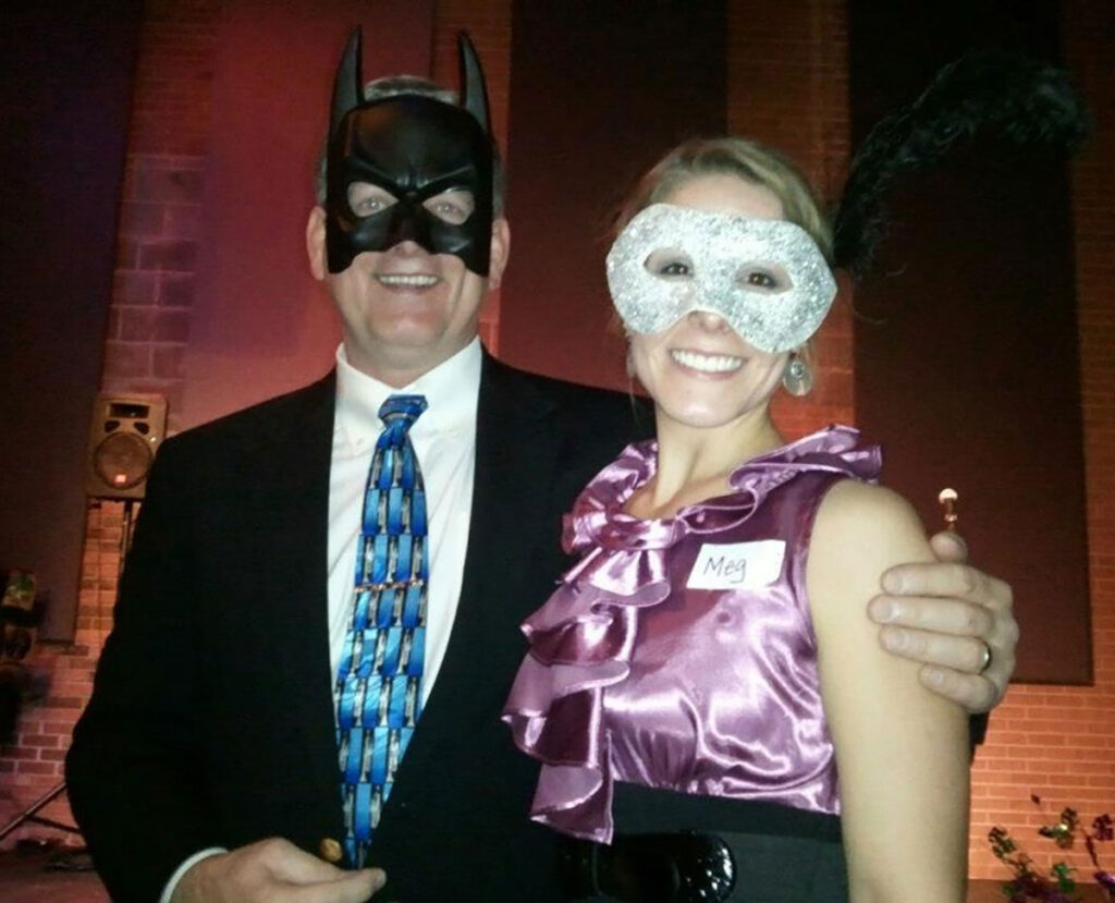 Two adults at a formal event wearing a Batman mask and silver eye mask.