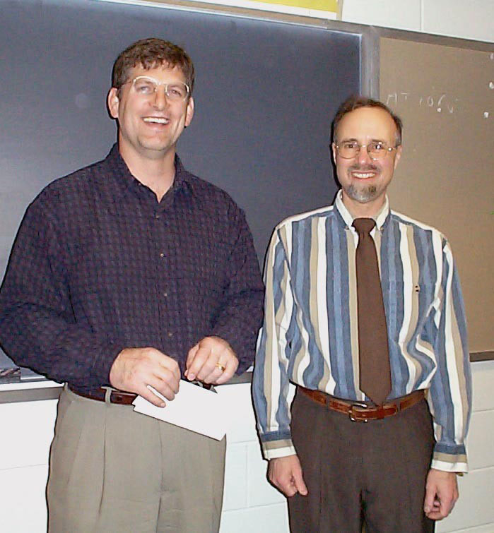 Two adults standing together in front of a blackboard.