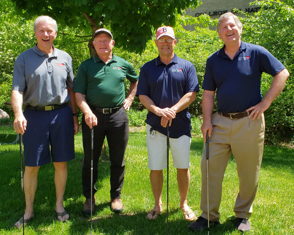 Four adults standing on grass holding golf clubs during an outdoor gathering.