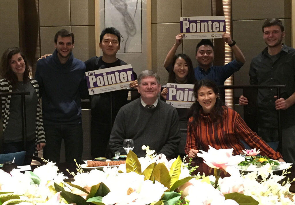 Group posing at a dining table while holding ‘I’m a Pointer’ signs.