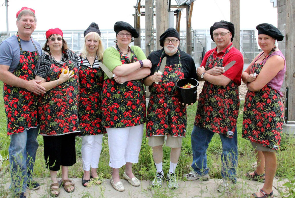Group wearing aprons and chef hats standing together inside a greenhouse.