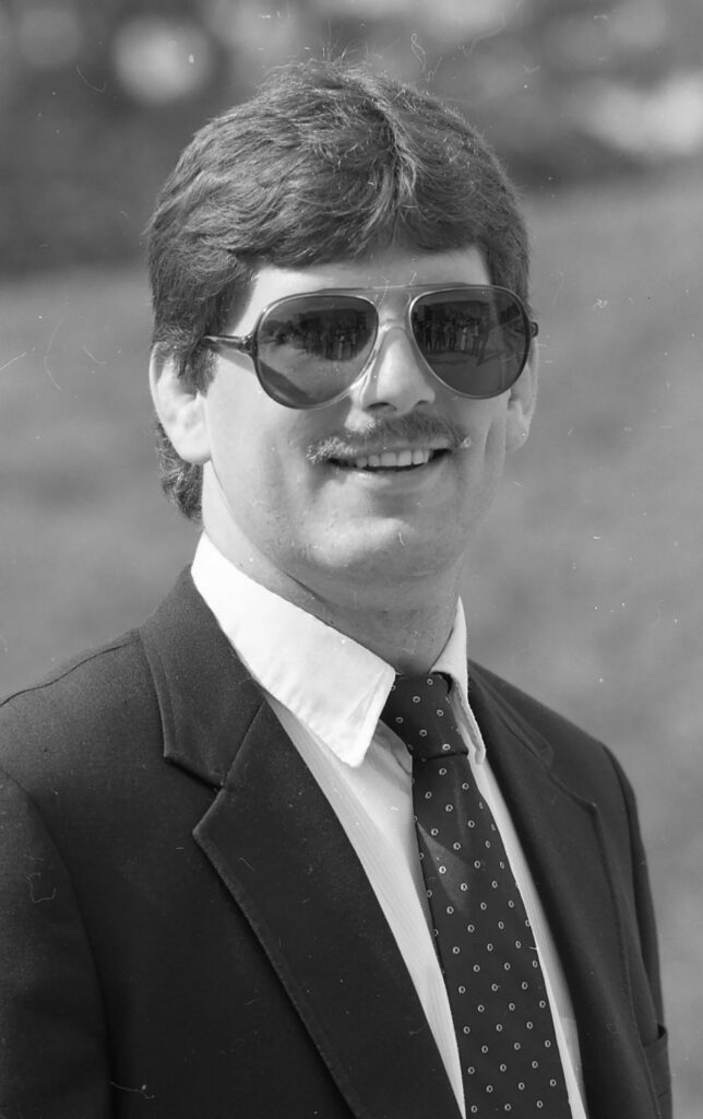Portrait of an adult in business attire photographed outdoors against a natural background.