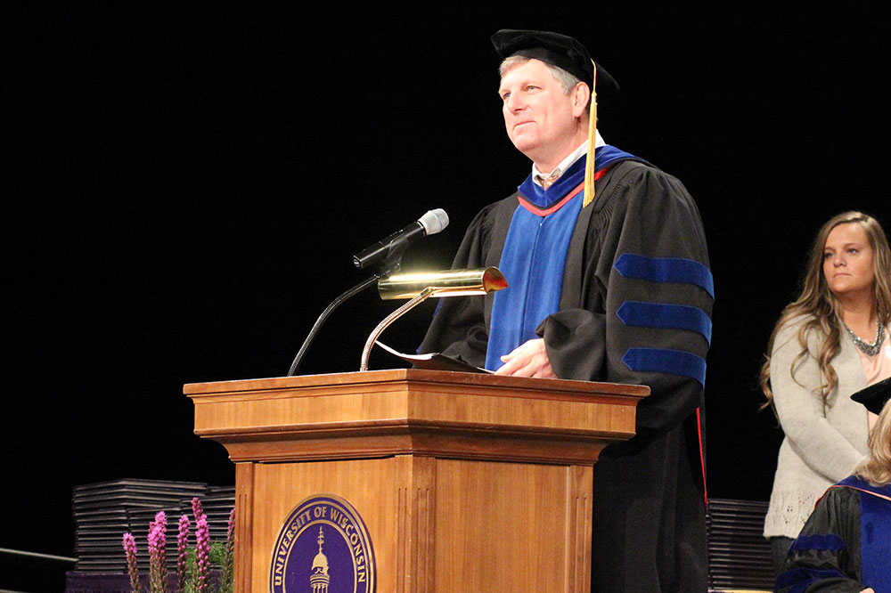 Faculty member speaking from a podium in academic regalia during a formal ceremony.