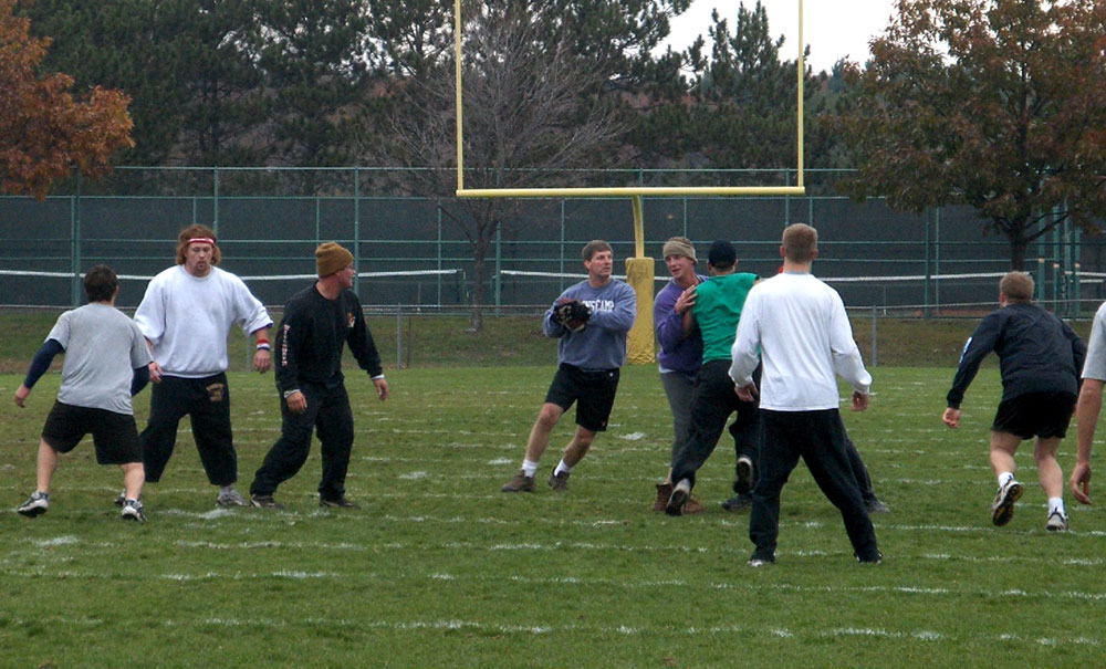 Group playing football on a grass field with goalposts in the background.