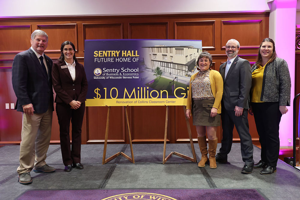 Group standing beside a display announcing Sentry Hall as a future home for Sentry School of Business and Economics.