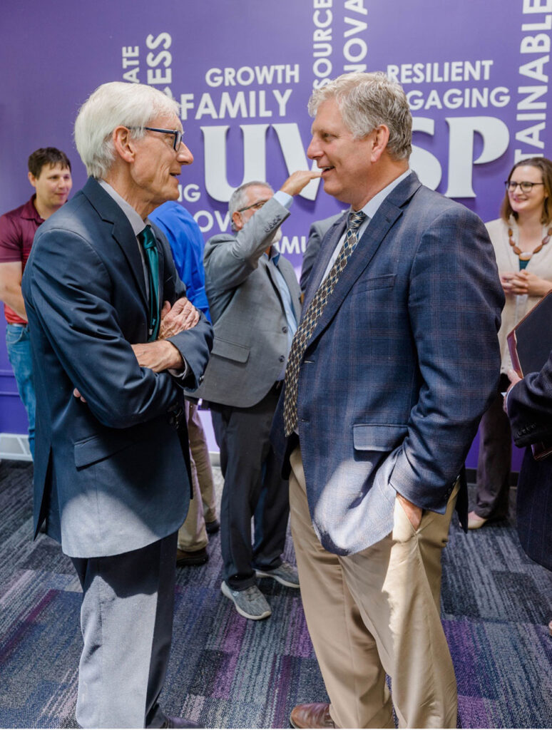 Faculty and governor standing together indoors at a professional event.