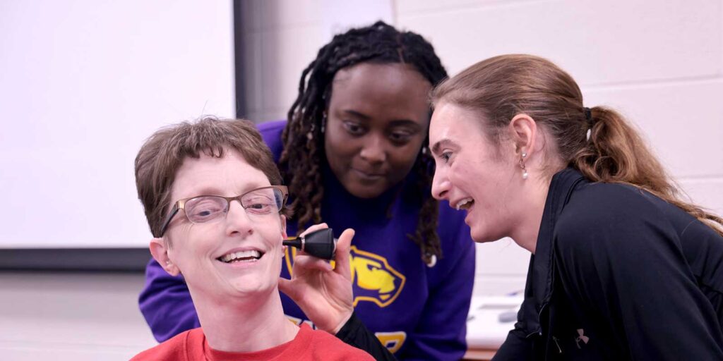 Two student clinicians check the hearing of a clinic patient.