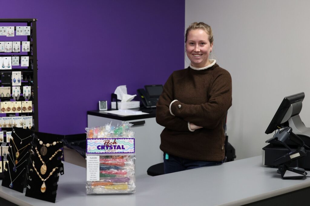 student stands with arms crossed at gift shop front desk