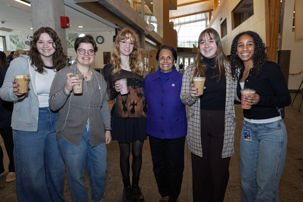 Group of six people with coffee posing for a photo in the concourse of the Dreyfus University Center.