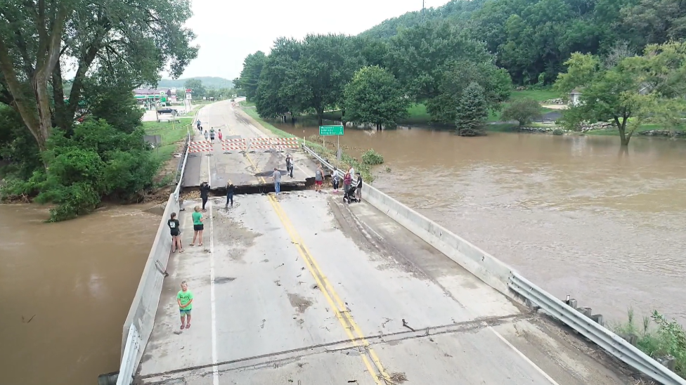 Black Earth state highway blocked off after severe flood damages. People standing on bridge and river shown.