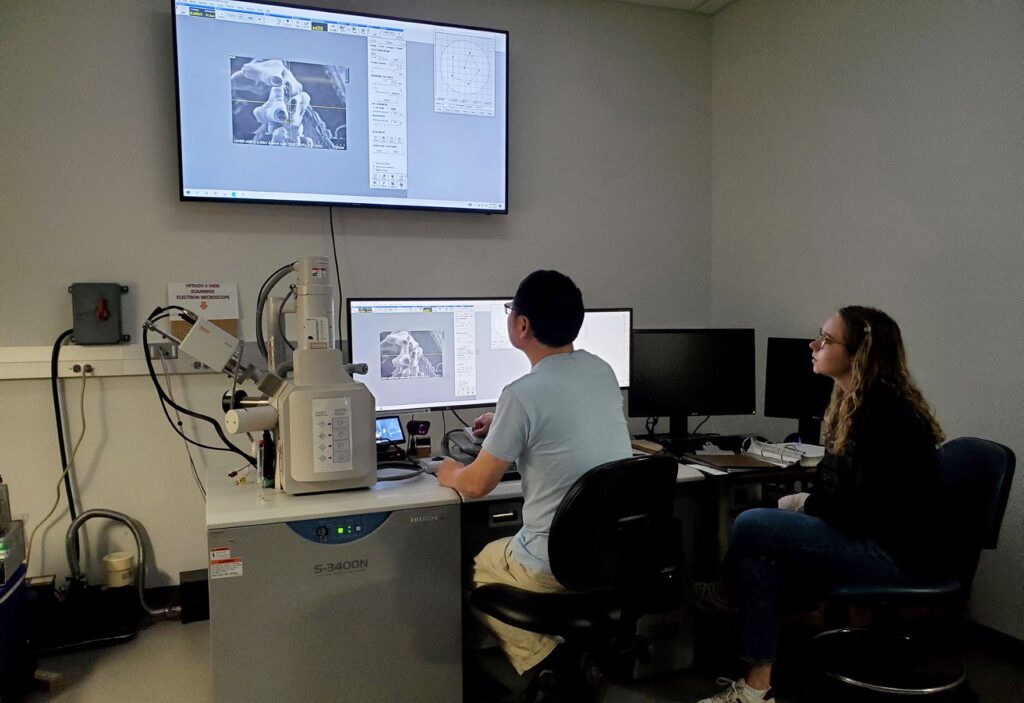 Student works with faculty member to study an image magnified in the SEM, scanning electron microscope.