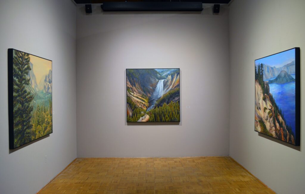 Gallery room displaying three landscape paintings of mountains, forests, water.