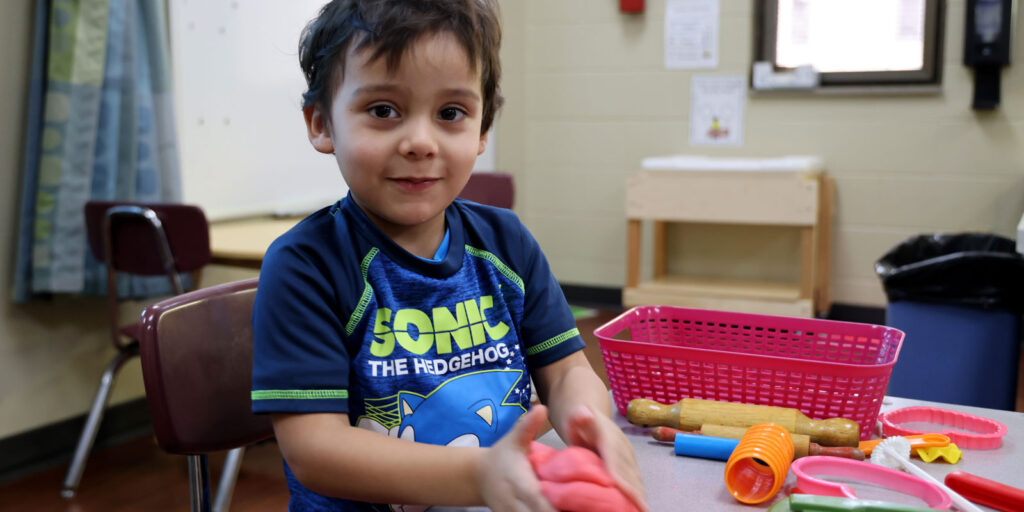 A young child playing with dough and toys sitting at a table.
