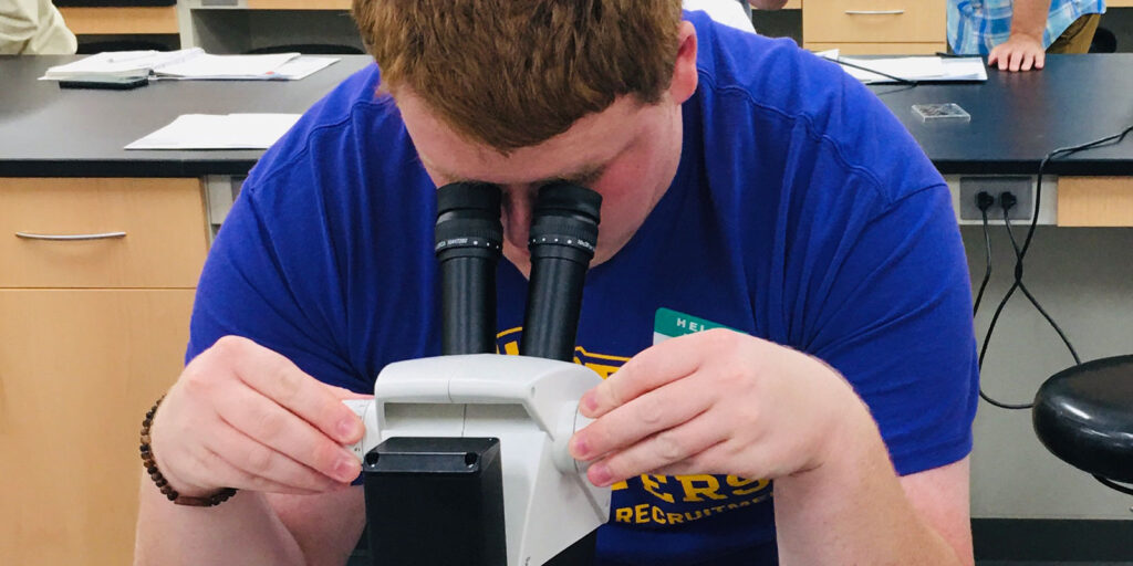 Student examining a microscope slide at a lab table during a WINSTEP science activity.