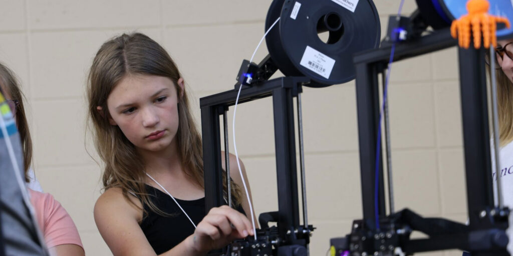 A student adjusts filament on a 3D printer while working on a STEAM project.