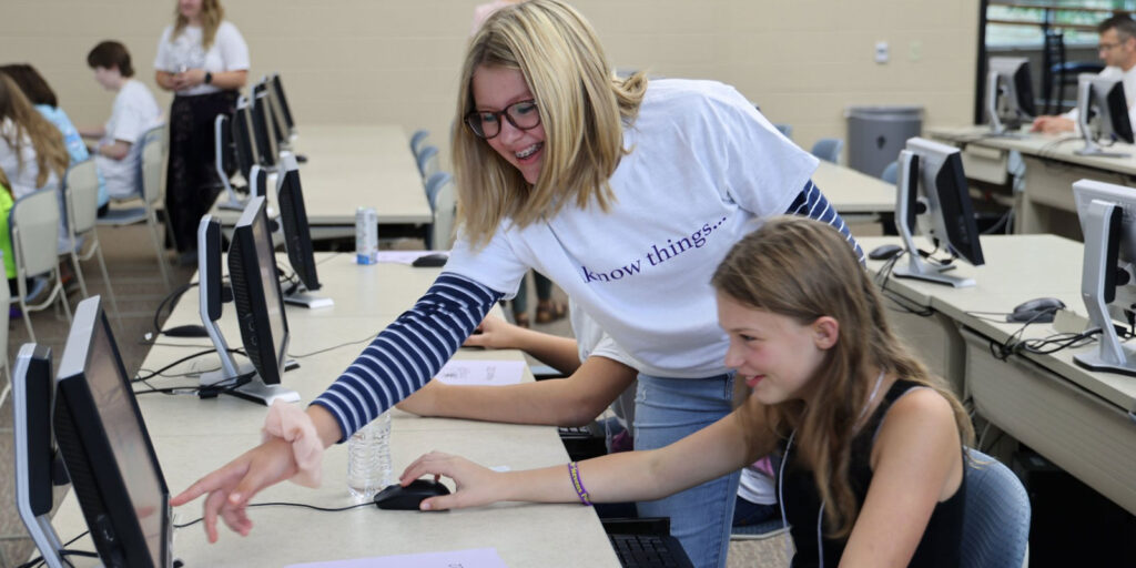 An instructor assists a student at a computer during a STEAM class activity.