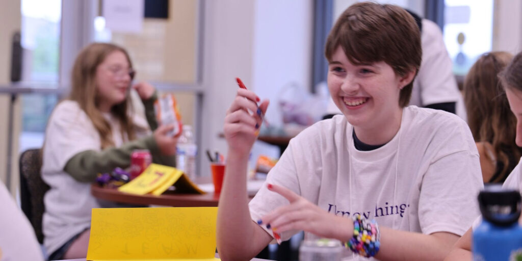 A student smiles while working on a STEAM activity in a classroom setting.