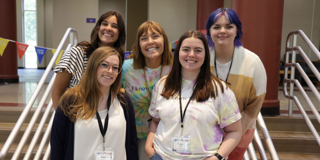 A small group of program leaders wearing event badges pose together on a staircase inside a building.