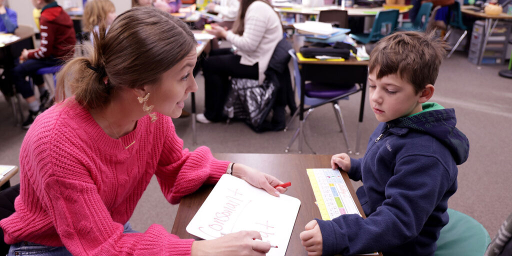 An educator works one-on-one with a student using a small whiteboard during a literacy lesson.