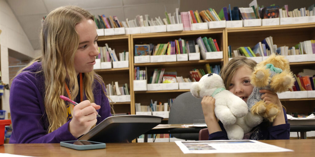 An educator meets with a student at a table using letter tiles during a literacy activity.
