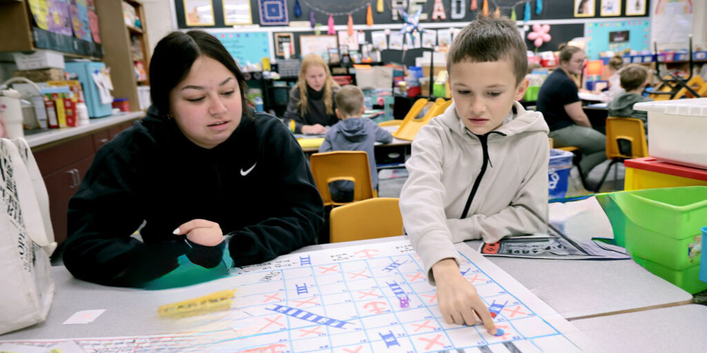 An educator meets with a student at a table using letter tiles during a literacy activity.