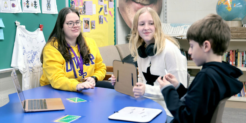 An educator works with two students at a table using white boards.