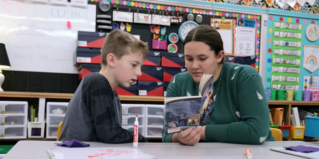 A student reads from a leveled reader book during a guided reading session.