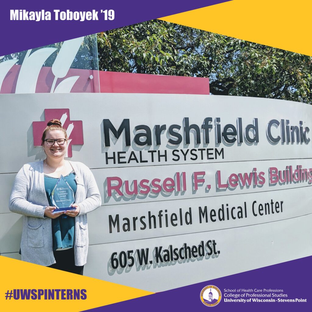 Person stands outside the Marshfield Clinic Russell F. Lewis Building holding an award.
