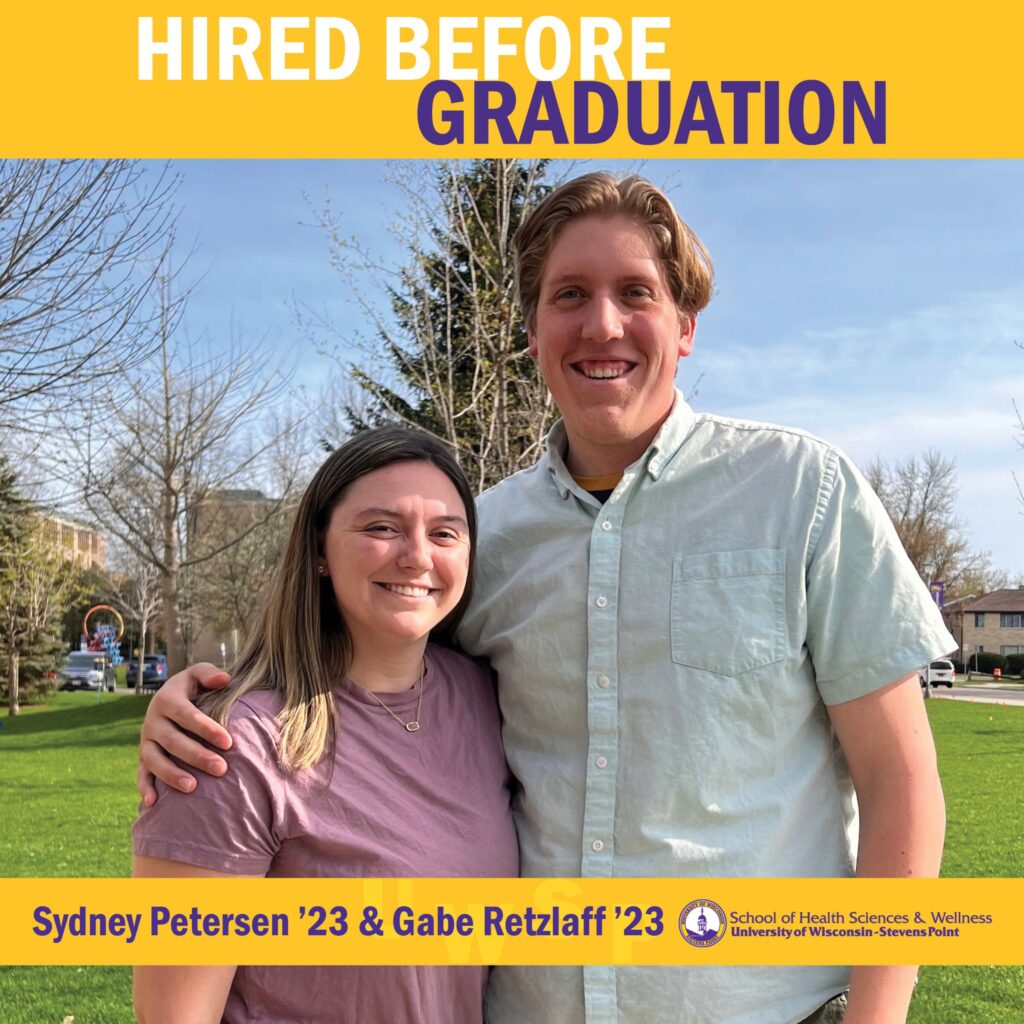 Two graduates stand arm in arm on a grassy campus lawn beneath the text “Hired Before Graduation.”