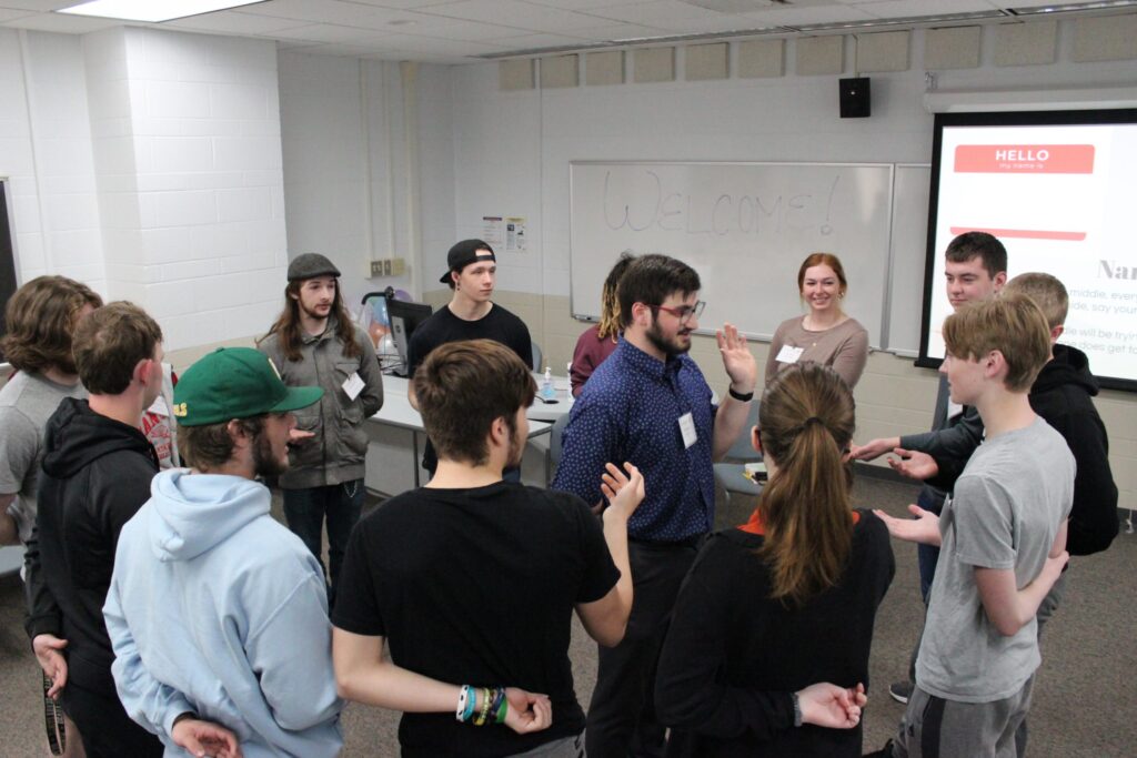 Connections Project  teaching student in center of room as other students raise their hands.