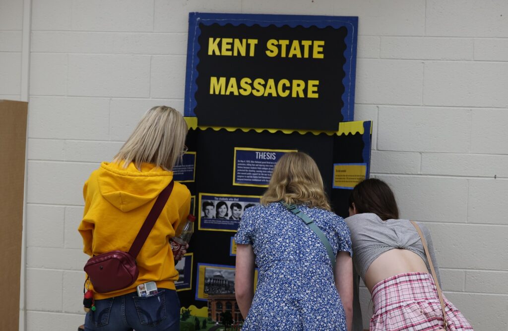 Kent State Massacre poster display with three people viewing the entries.