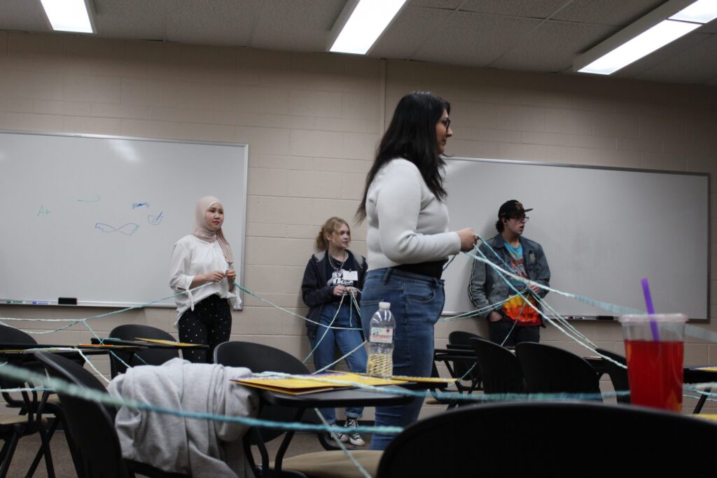 Connections Project teaching student in center of room as other students hold yarn