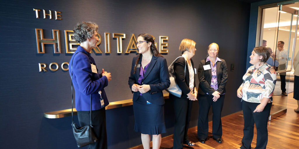 Attendees conversing in front of The Heritage Room sign before an event