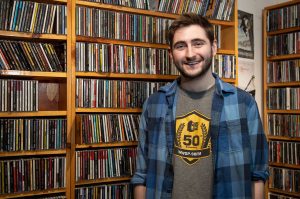 A student posing in front of CDs in 90FM Radio Station.