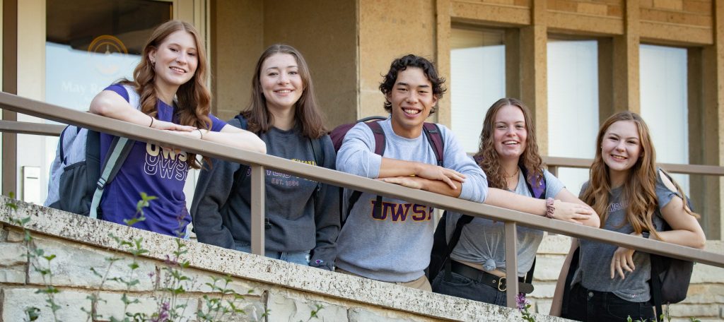 Four female and one male smiling by the residence hall ramp.