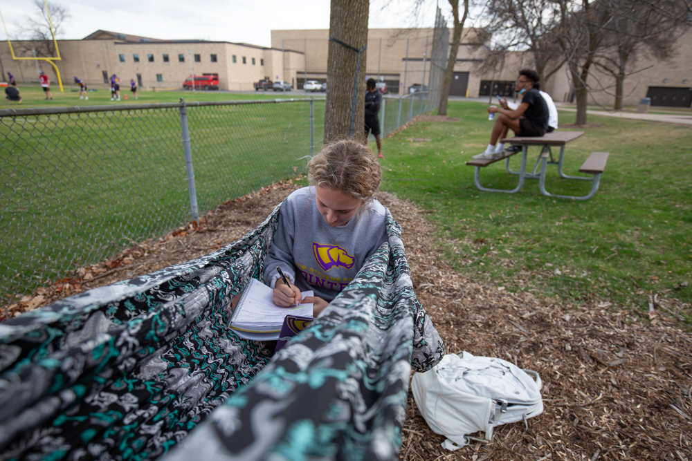 A female student taking notes in a hammock on campus.