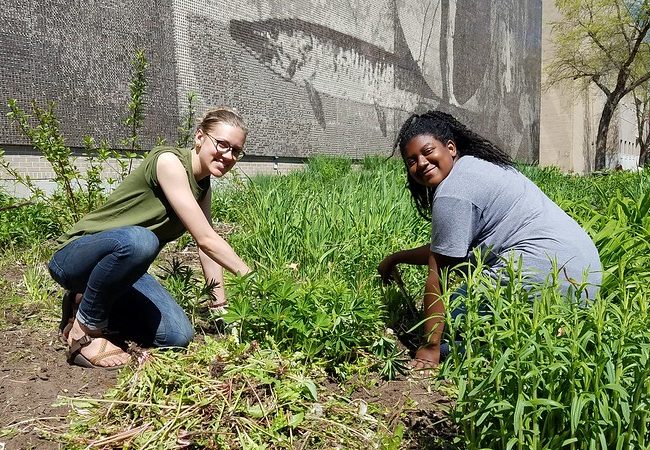 Two students planting in front of our mural on campus.