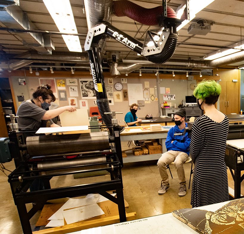 Professor and students learning printmaking on the press