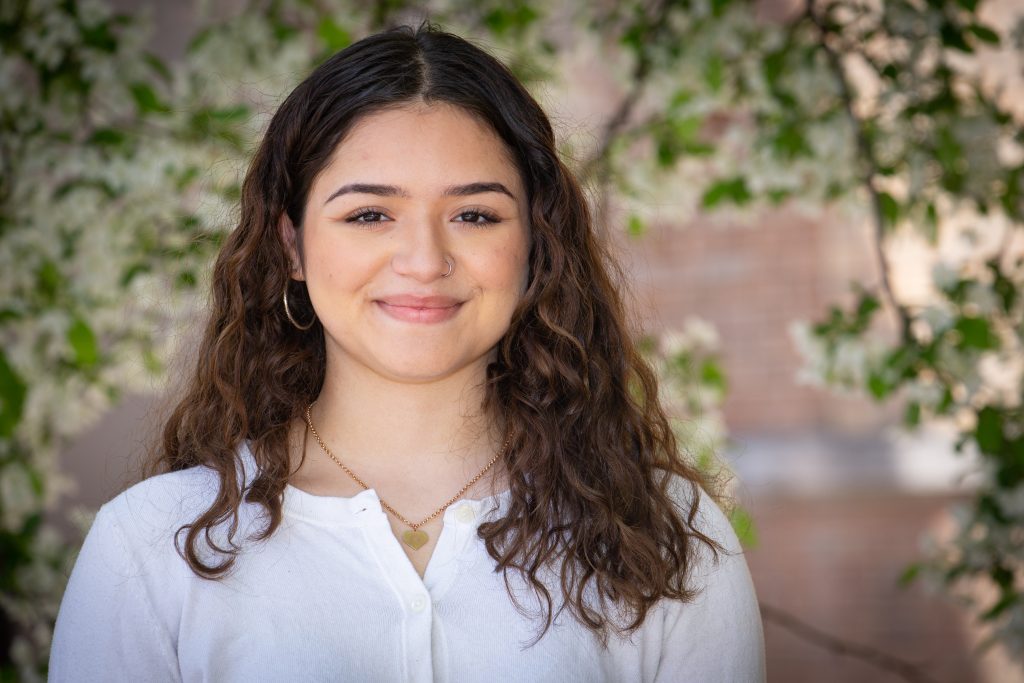 Student smiling by a blossoming tree next to the Communication Arts Center.