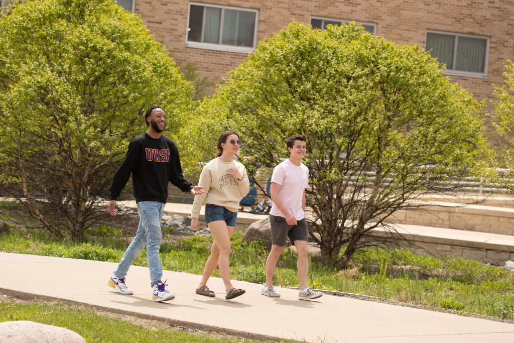 Three students walking on the sidewalk by residence halls.