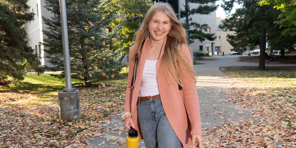 Student walking on the sidewalk on a fall day.