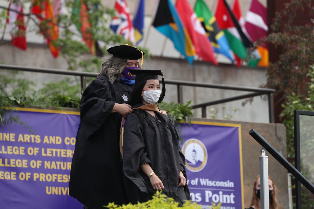 Graduate student being hooded at outside Spring Commencement by faculty member.